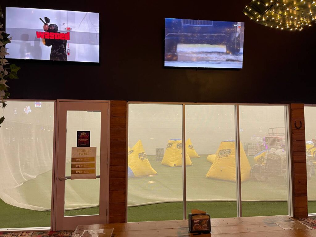 Indoor Paintball Field Viewed Through Large Glass Panels with TVs Above